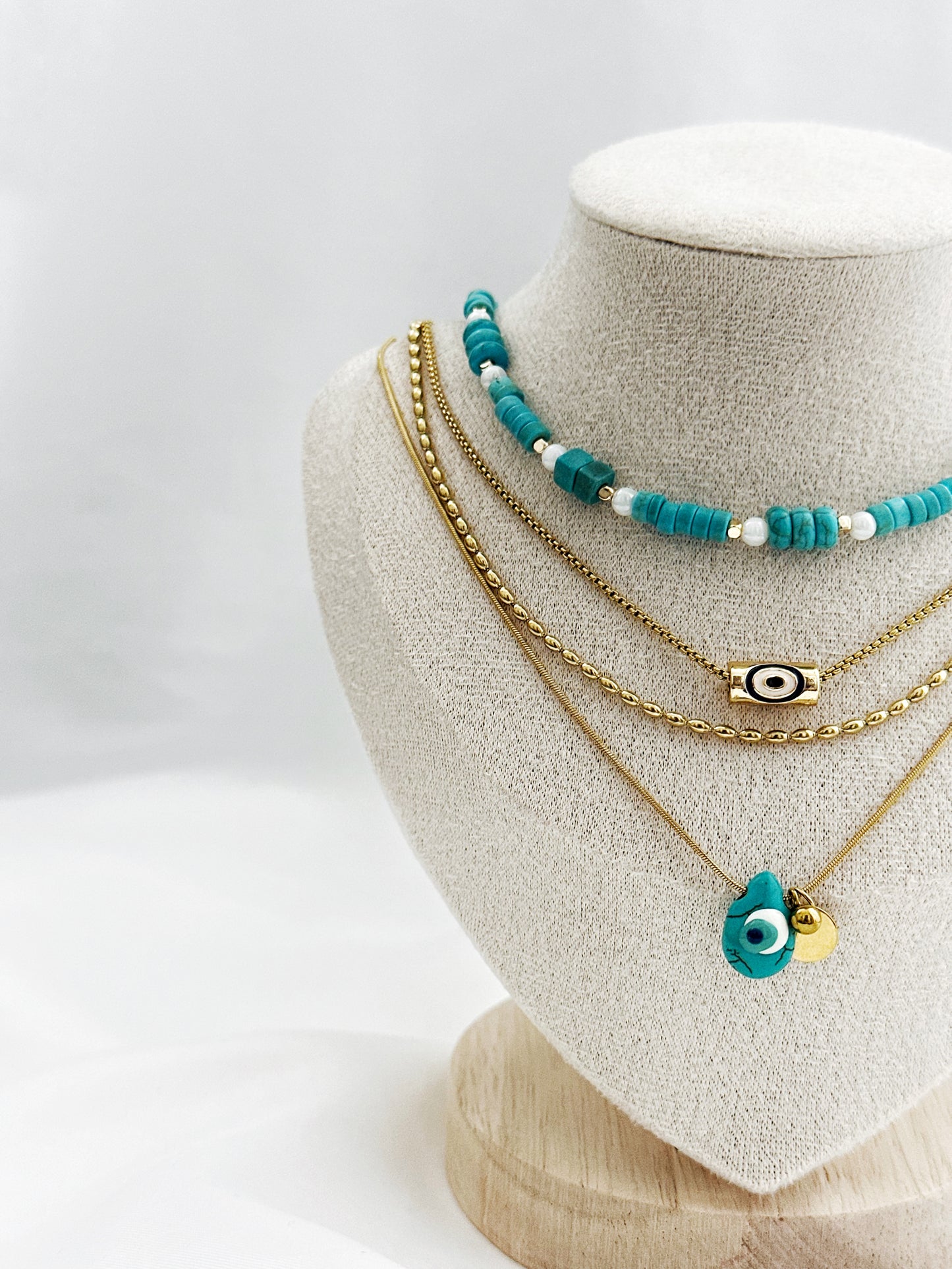 4-lagiges Layering-Kettenset auf hellem Untergrund – bestehend aus goldenen Edelstahlketten mit Nazar-Amuletten, echter Türkis- und Perlmuttkette im Boho-Stil