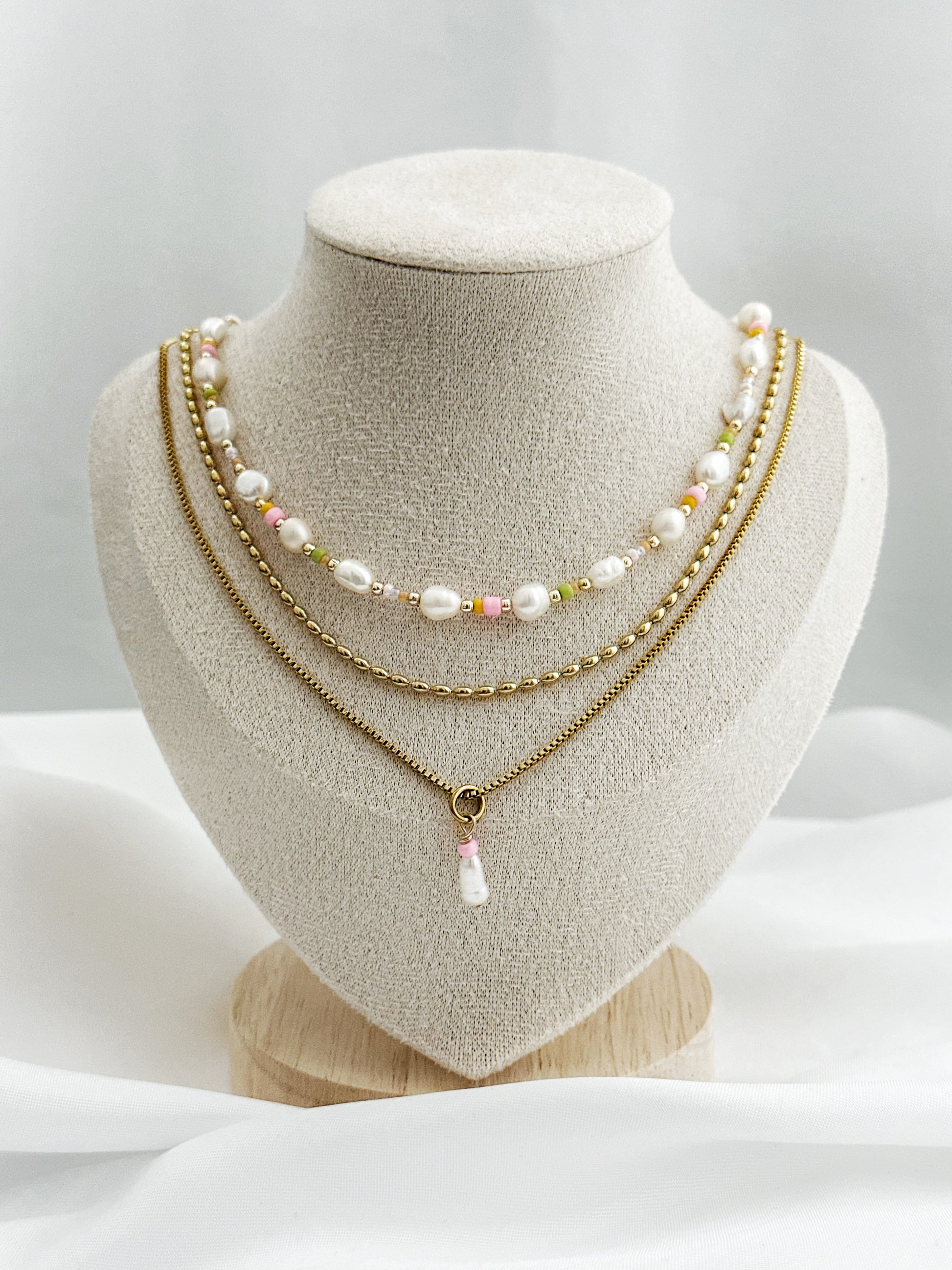 Dreiteiliges Layering-Kettenset mit goldenen Details, Süßwasserperlen und farbigen Akzenten auf Schmuckständer – wählbar in zwei Varianten.