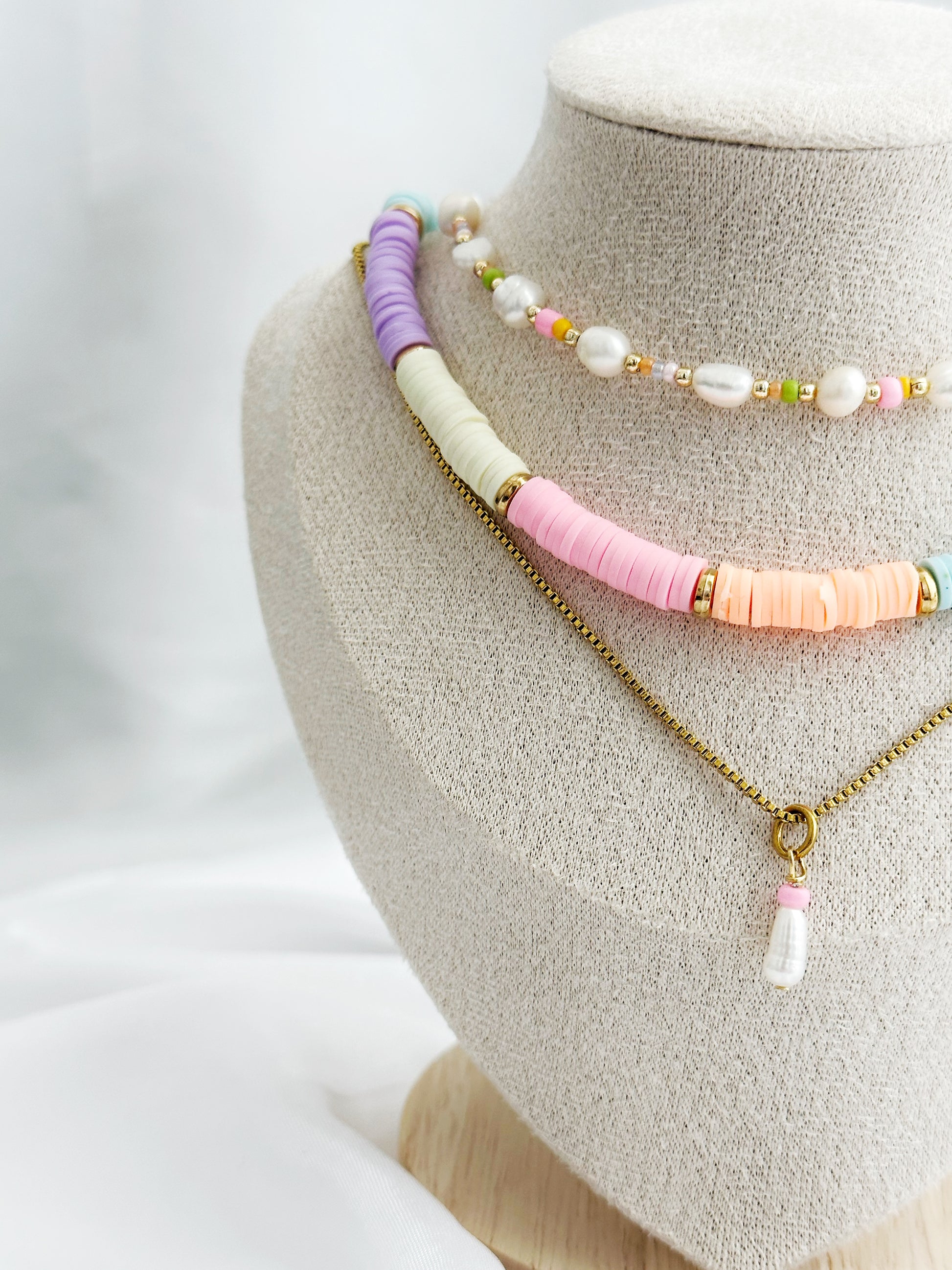 Dreiteiliges Layering-Kettenset mit Süßwasserperlen, bunten Perlen und goldenen Details – flach arrangiert auf hellem Untergrund im Sommerstil