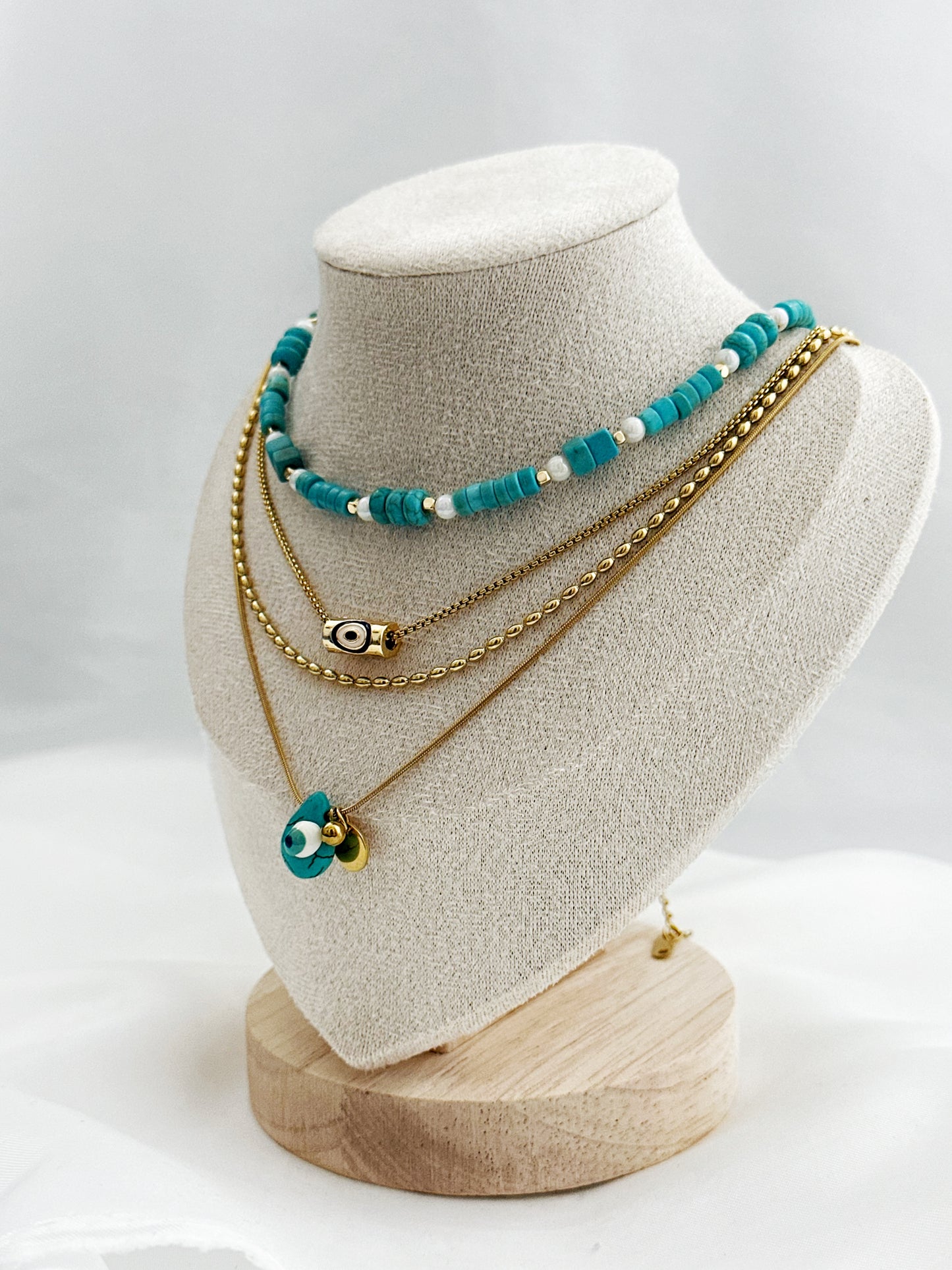 4-lagiges Layering-Kettenset auf hellem Untergrund – bestehend aus goldenen Edelstahlketten mit Nazar-Amuletten, echter Türkis- und Perlmuttkette im Boho-Stil