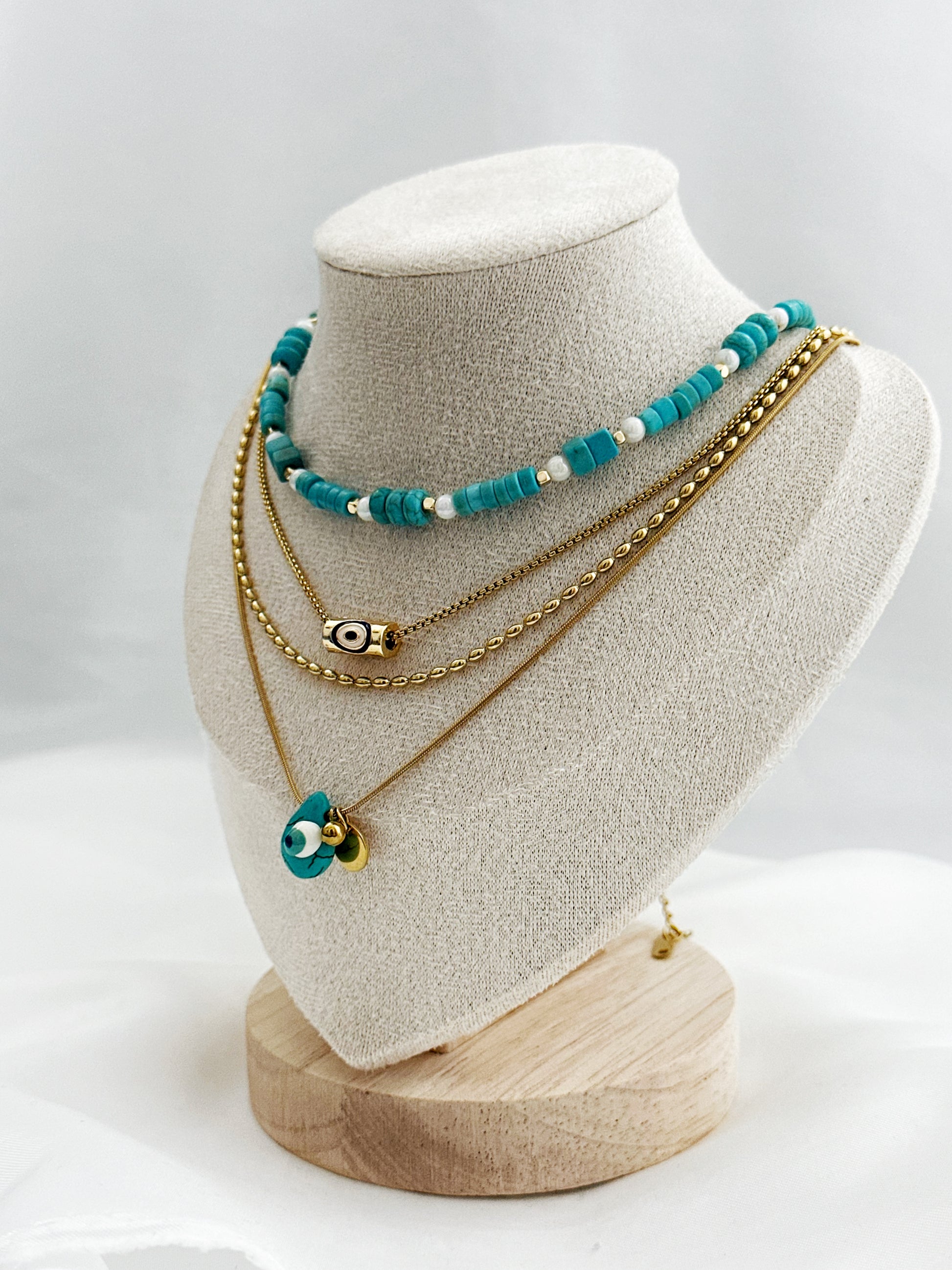 4-lagiges Layering-Kettenset auf hellem Untergrund – bestehend aus goldenen Edelstahlketten mit Nazar-Amuletten, echter Türkis- und Perlmuttkette im Boho-Stil