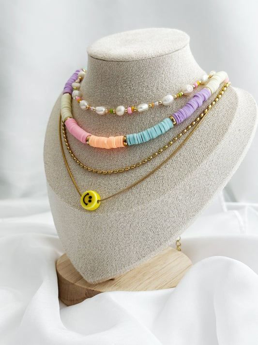 Vierlagiges Layering-Kettenset mit bunten Perlen, Süßwasserperlen, goldener Kette und Smiley-Anhänger – flach fotografiert auf hellem Hintergrund im Sommerstil