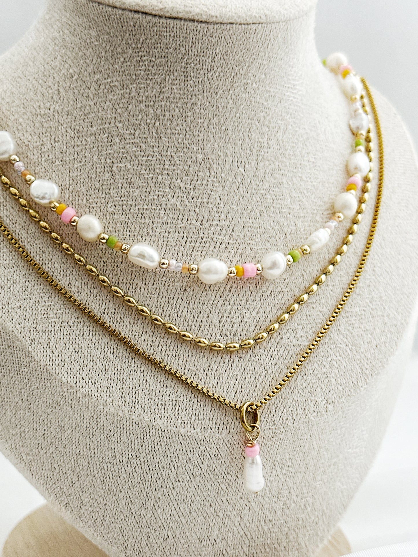 Dreiteiliges Layering-Kettenset mit goldenen Details, Süßwasserperlen und farbigen Akzenten auf Schmuckständer – wählbar in zwei Varianten.