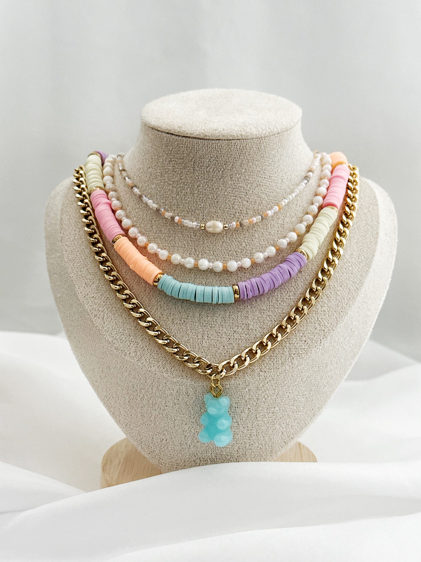 Layering-Set mit vier Halsketten: Perlenkette in Rosé, bunte Perlenkette, bunte Heishi-Perlenkette und goldene Panzerkette mit Gummibärchen-Anhänger