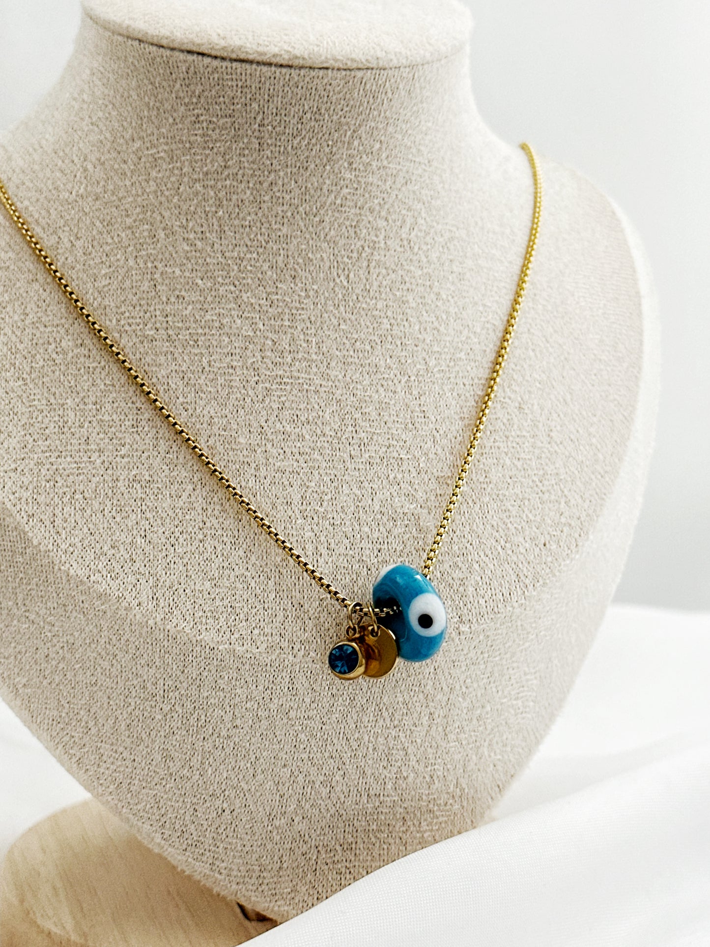 Goldene Edelstahlkette mit drei Anhängern – blauer Glitzerstein, rundes Plättchen und Nazar Auge in Dreiecksform, 45 cm lang