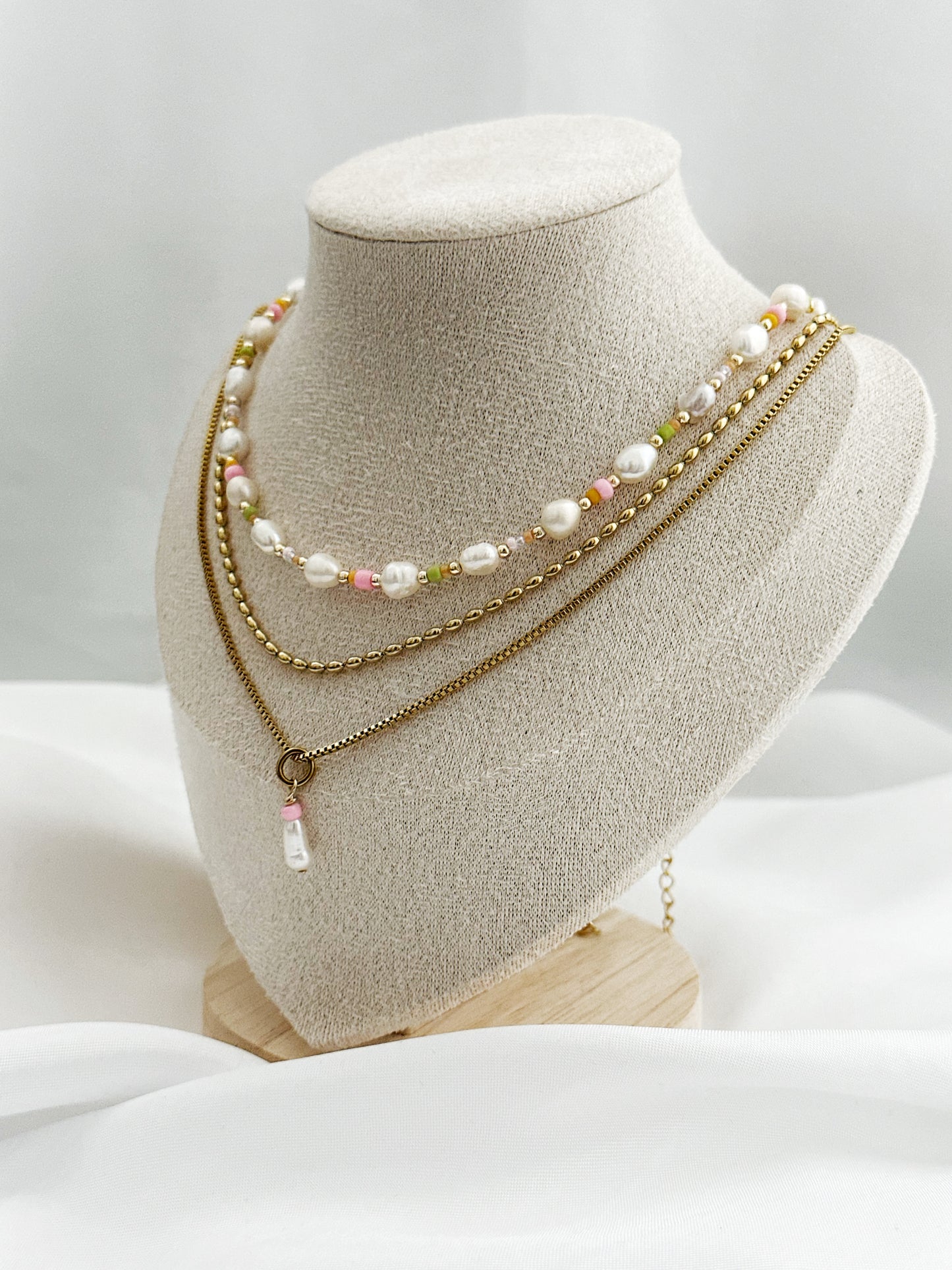 Dreiteiliges Layering-Kettenset mit goldenen Details, Süßwasserperlen und farbigen Akzenten auf Schmuckständer – wählbar in zwei Varianten.