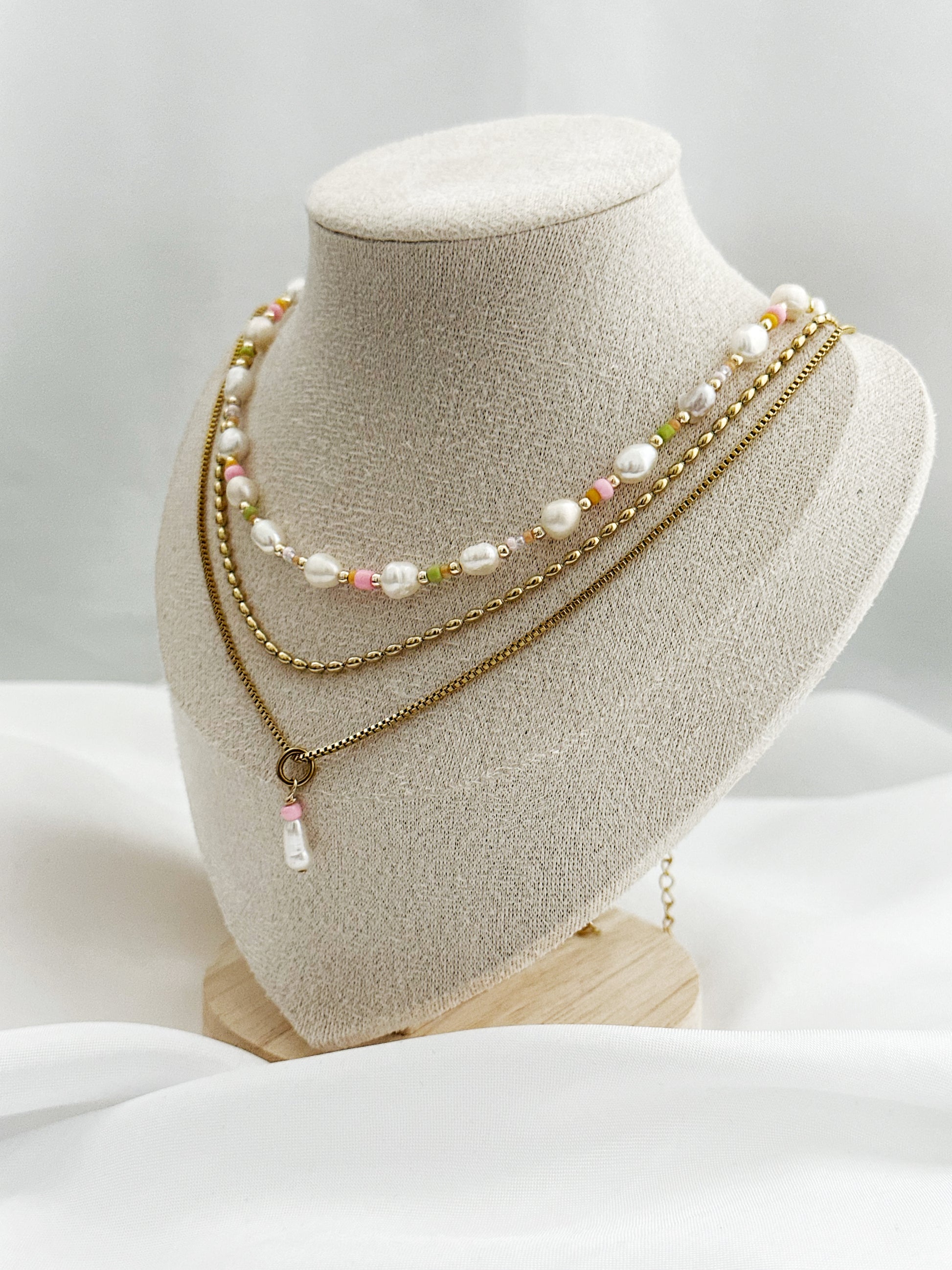 Dreiteiliges Layering-Kettenset mit goldenen Details, Süßwasserperlen und farbigen Akzenten auf Schmuckständer – wählbar in zwei Varianten.