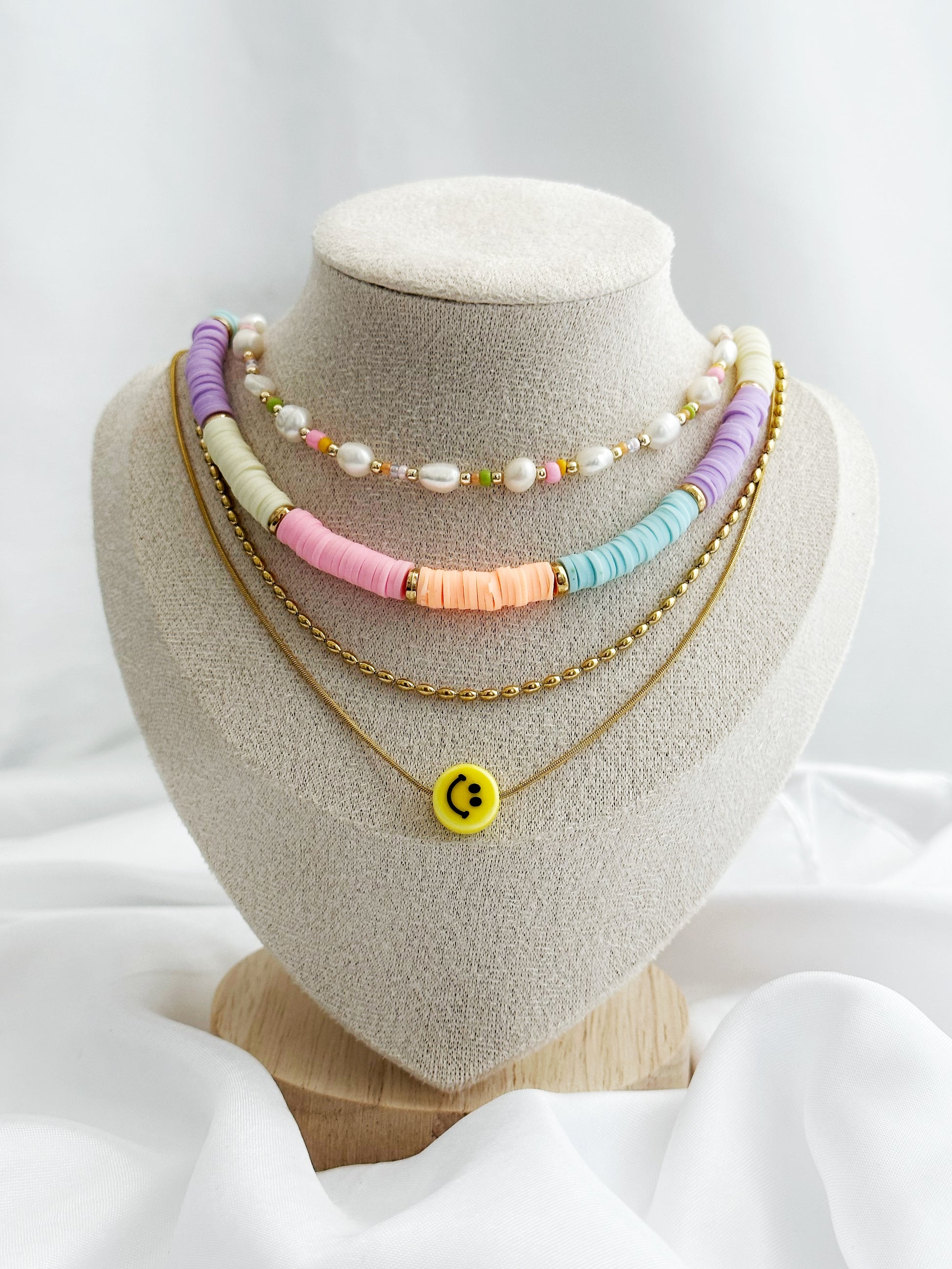 Vierlagiges Layering-Kettenset mit bunten Perlen, Süßwasserperlen, goldener Kette und Smiley-Anhänger – flach fotografiert auf hellem Hintergrund im Sommerstil
