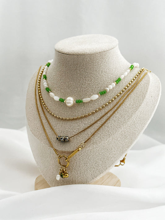 Goldenes Layering-Ketten-Set für Damen, mit Süßwasserperlen, Nazar-Augen, grünen Perlen und Anhängern – stilvoll arrangiert auf einem Schmuckständer