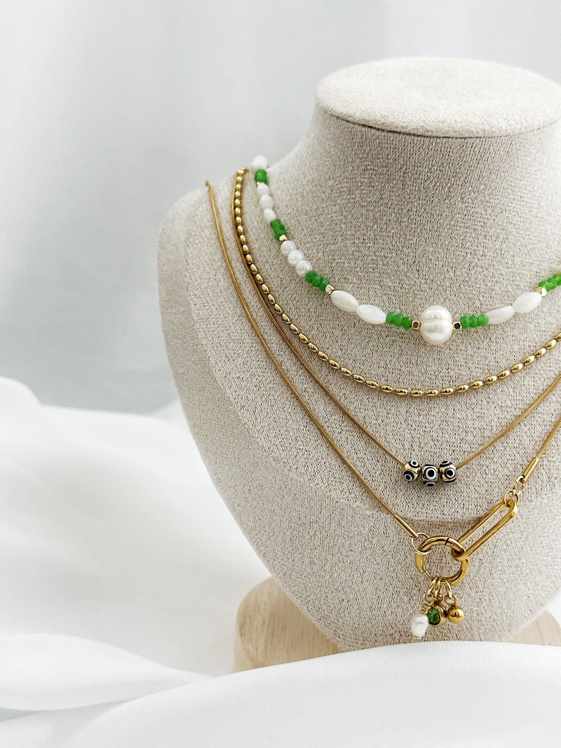 Goldenes Layering-Ketten-Set für Damen, mit Süßwasserperlen, Nazar-Augen, grünen Perlen und Anhängern – stilvoll arrangiert auf einem Schmuckständer