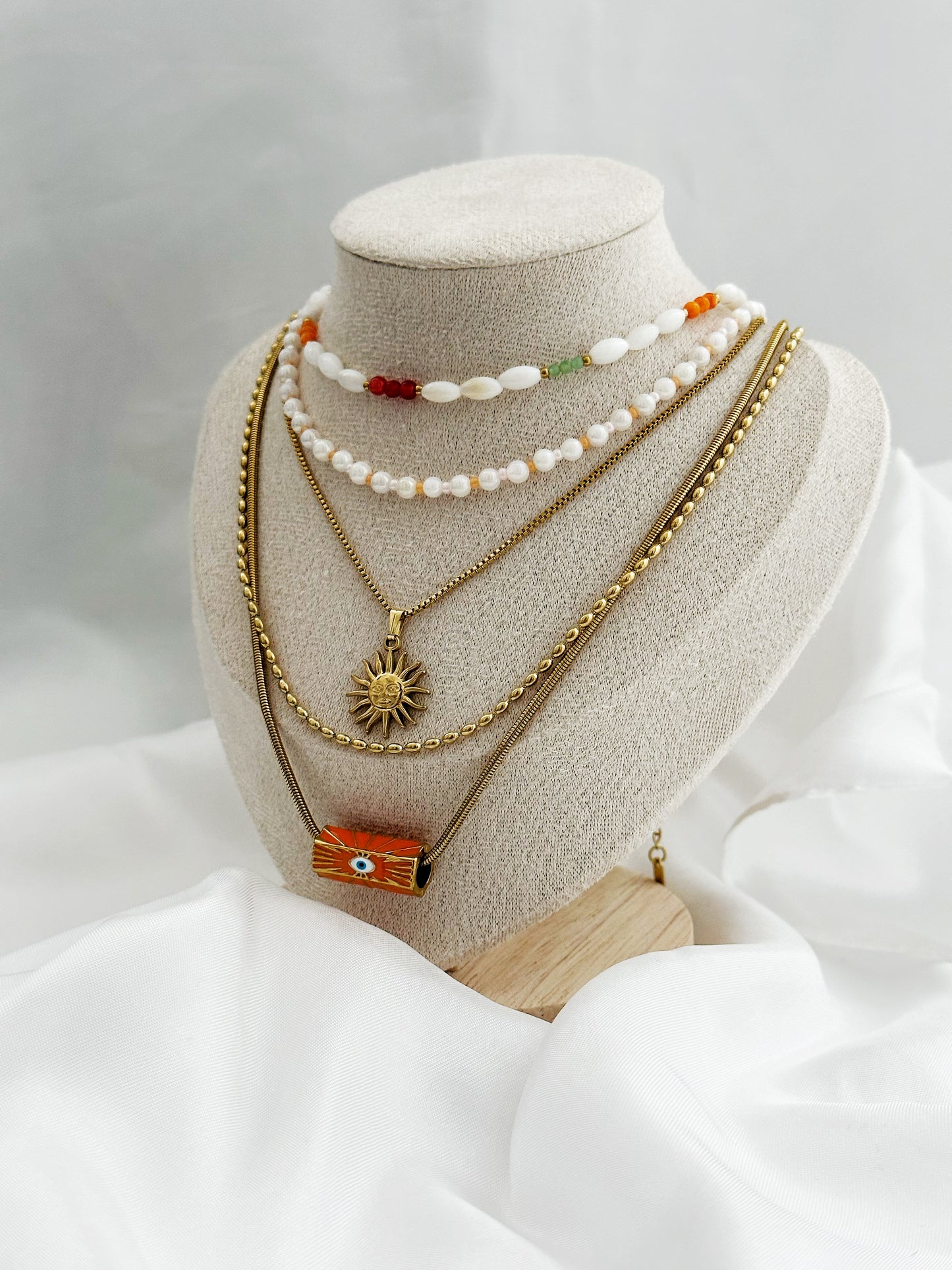 Layering-Ketten-Set mit fünf goldfarbenen und perlenbesetzten Halsketten. Mit Sonnen-Anhänger, Nazar-Auge und natürlichen Perlen in Weiß, Orange und Gold