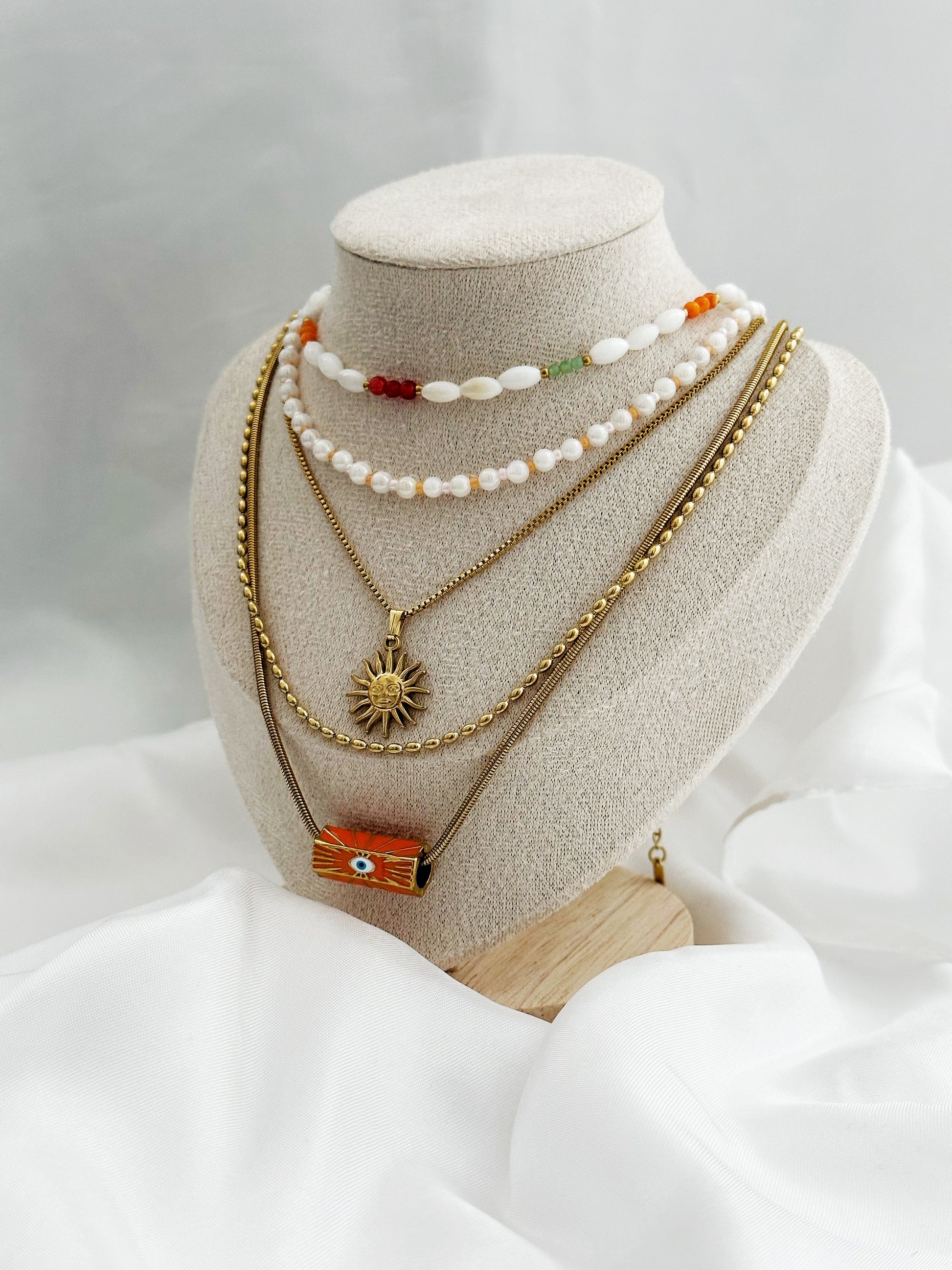 Layering-Ketten-Set mit fünf goldfarbenen und perlenbesetzten Halsketten. Mit Sonnen-Anhänger, Nazar-Auge und natürlichen Perlen in Weiß, Orange und Gold