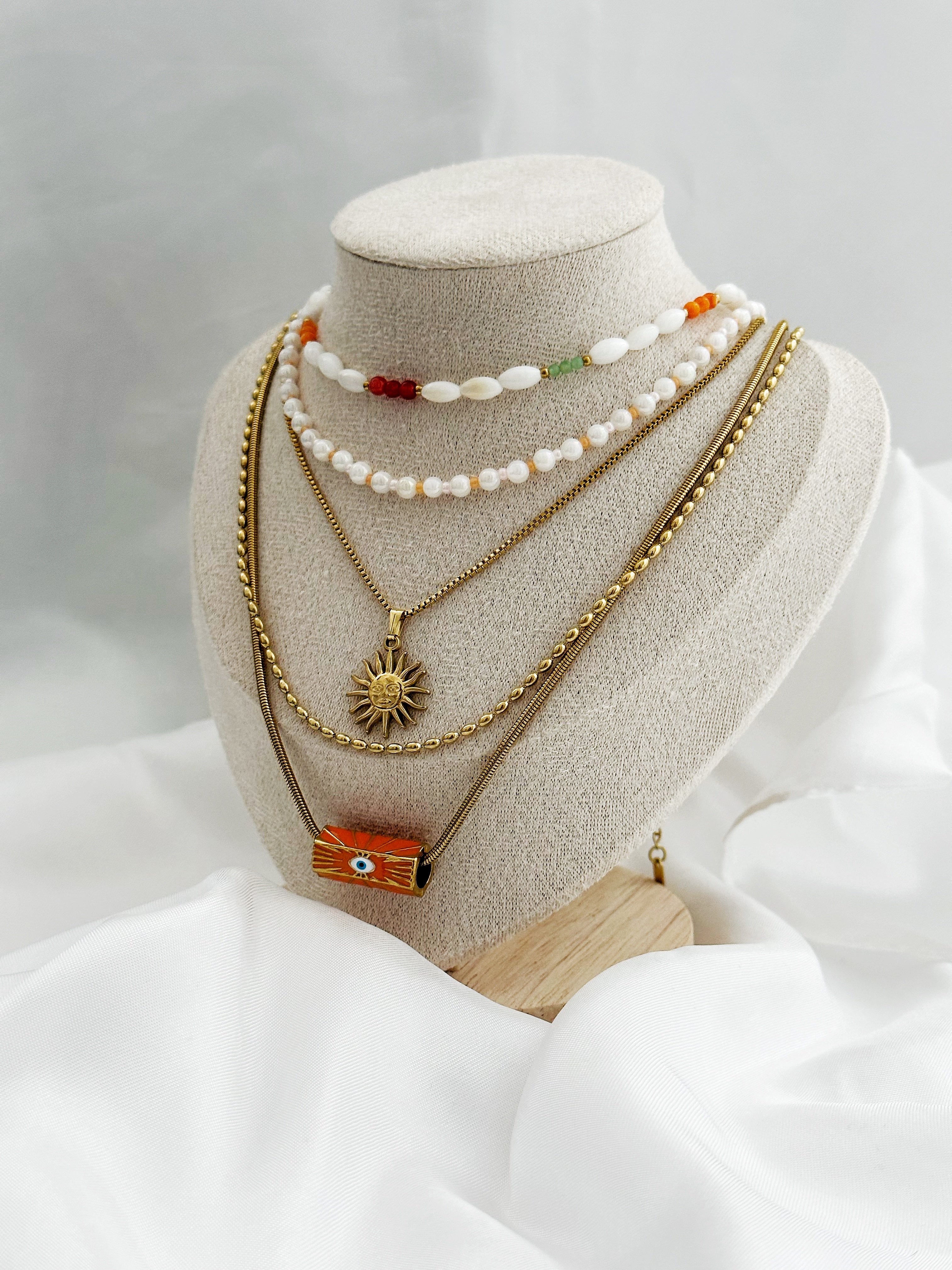 Layering-Ketten-Set mit fünf goldfarbenen und perlenbesetzten Halsketten. Mit Sonnen-Anhänger, Nazar-Auge und natürlichen Perlen in Weiß, Orange und Gold