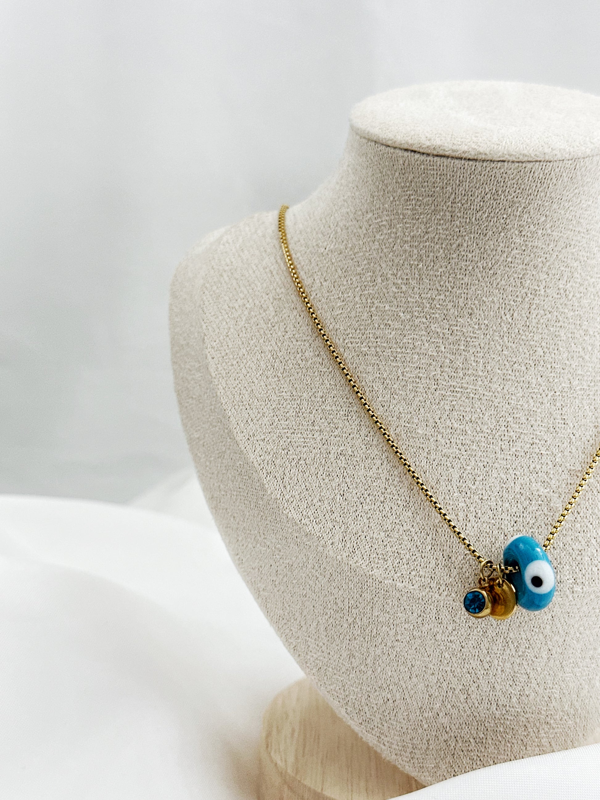 Goldene Edelstahlkette mit drei Anhängern – blauer Glitzerstein, rundes Plättchen und Nazar Auge in Dreiecksform, 45 cm lang