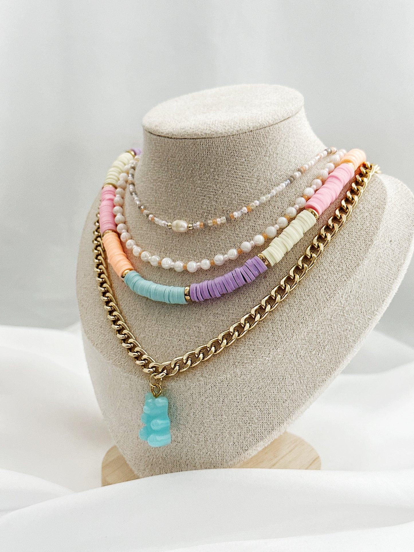 Layering-Set mit vier Halsketten: Perlenkette in Rosé, weiße Perlenkette, bunte Fimo-Perlenkette und goldene Panzerkette mit Gummibärchen-Anhänger