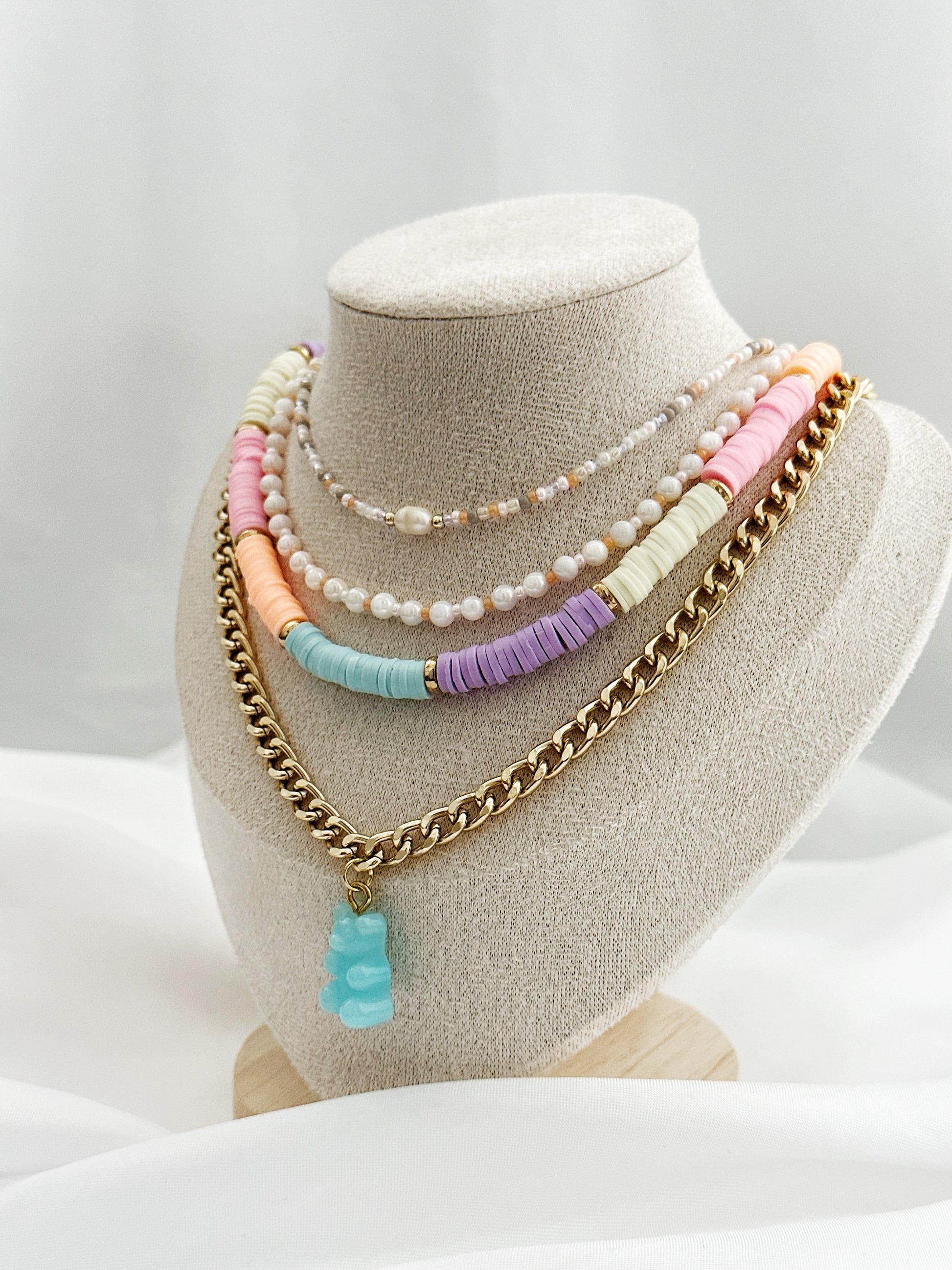 Layering-Set mit vier Halsketten: Perlenkette in Rosé, weiße Perlenkette, bunte Fimo-Perlenkette und goldene Panzerkette mit Gummibärchen-Anhänger