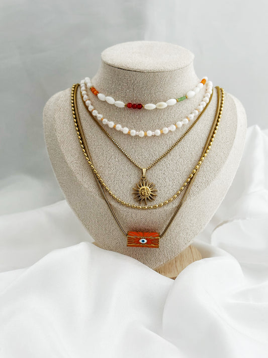 Layering-Ketten-Set mit fünf goldfarbenen und perlenbesetzten Halsketten auf Schmuckständer. Mit Sonnen-Anhänger, Nazar-Auge und natürlichen Perlen in Weiß, Orange und Gold