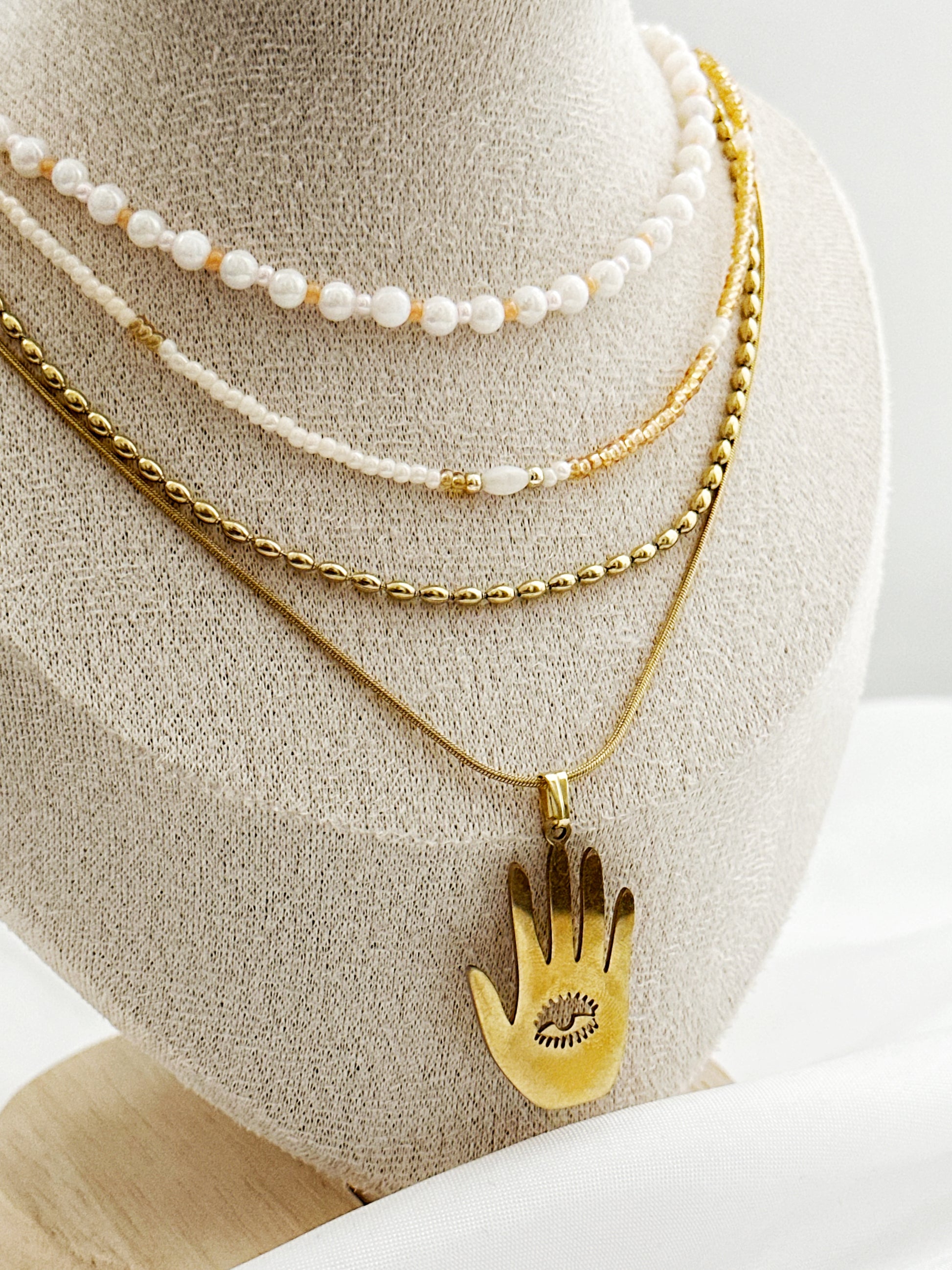 Elegantes Layering-Ketten-Set mit Hamsa-Anhänger, Süßwasserperlen und goldfarbenen Ketten auf Schmuckständer – 4-lagiger Schmucklook für Damen.