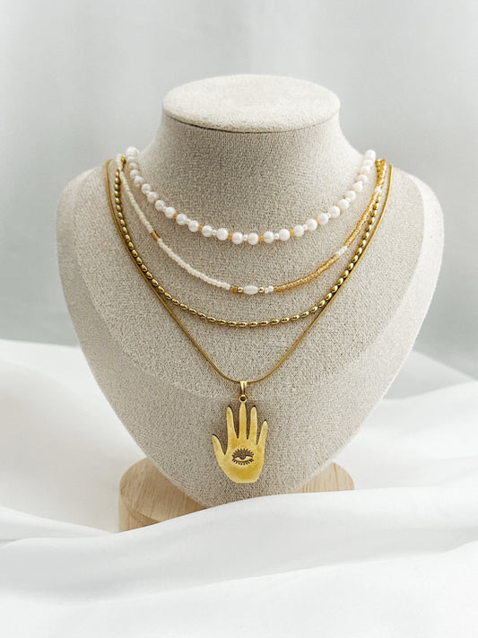 Elegantes Layering-Ketten-Set mit Hamsa-Anhänger, Süßwasserperlen und goldfarbenen Ketten auf Schmuckständer – 4-lagiger Schmucklook für Damen.