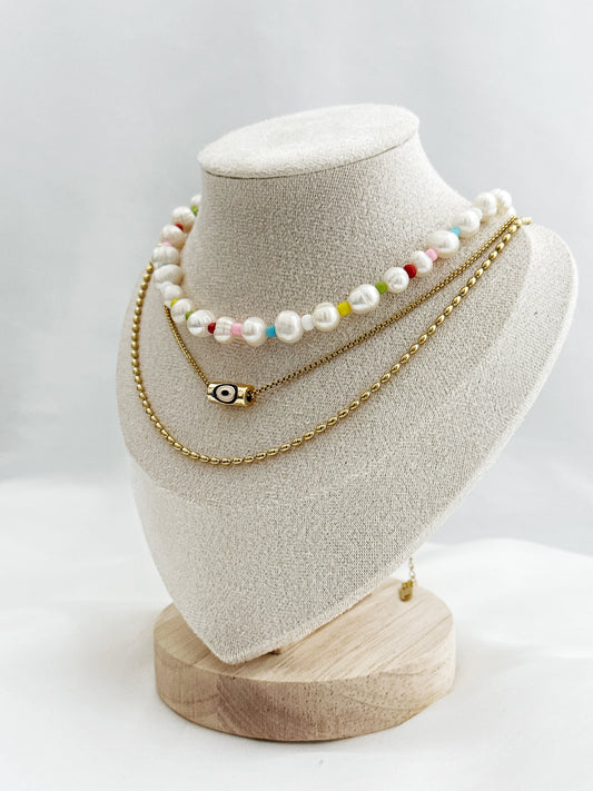 3-lagiges Kettenset mit unregelmäßigen Süßwasserperlen, bunter Perlenkette, Nazar-Anhänger und goldener Gliederkette – flach auf hellem Hintergrund arrangiert