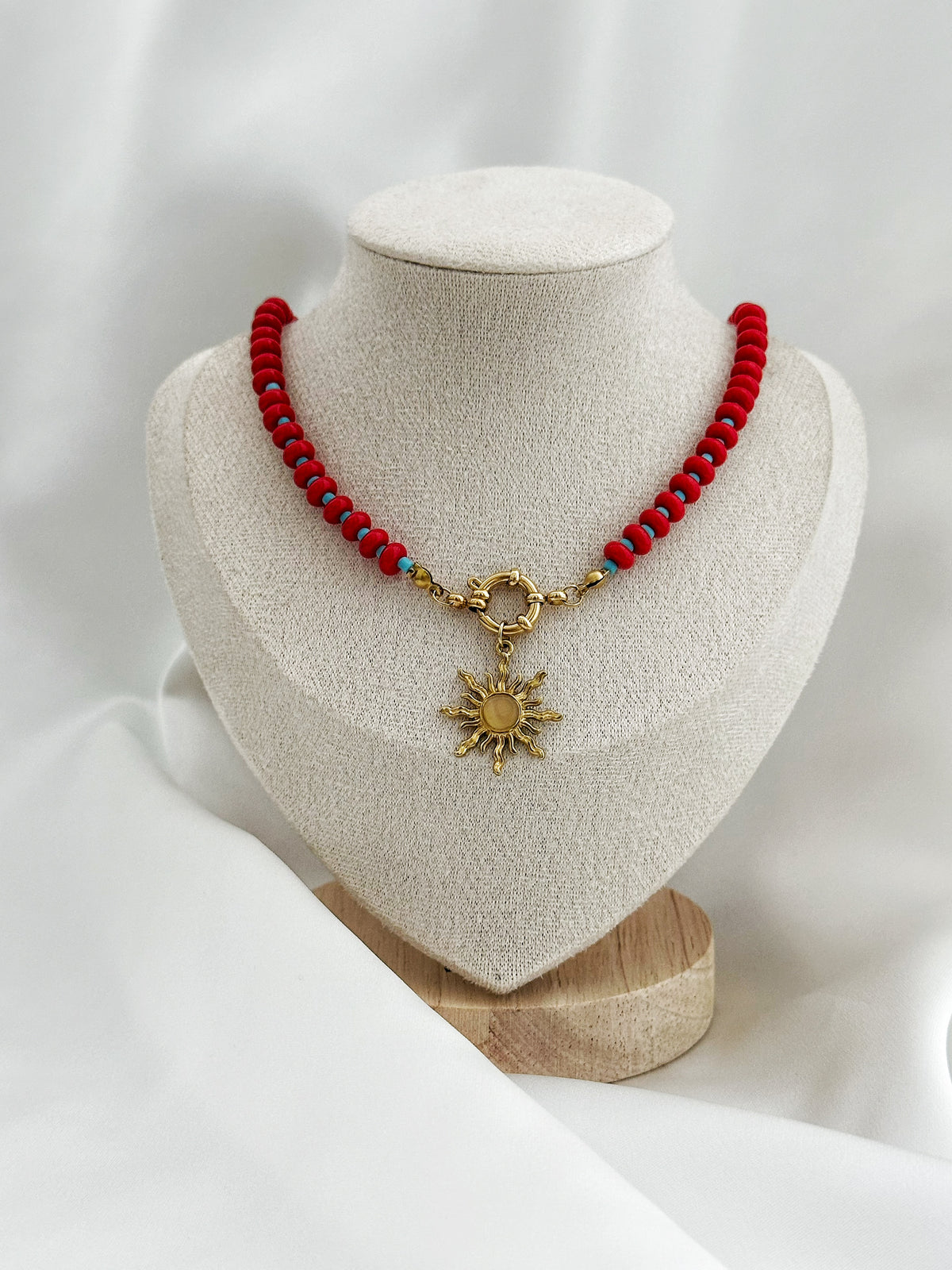 Rote und türkise Perlenkette mit Sonnenanhänger
Statement Perlenkette mit goldfarbenem Anhänger
Detailaufnahme der roten und türkisen Perlen